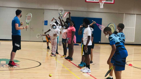 groups of kids in indoor gym learning about playing tennis